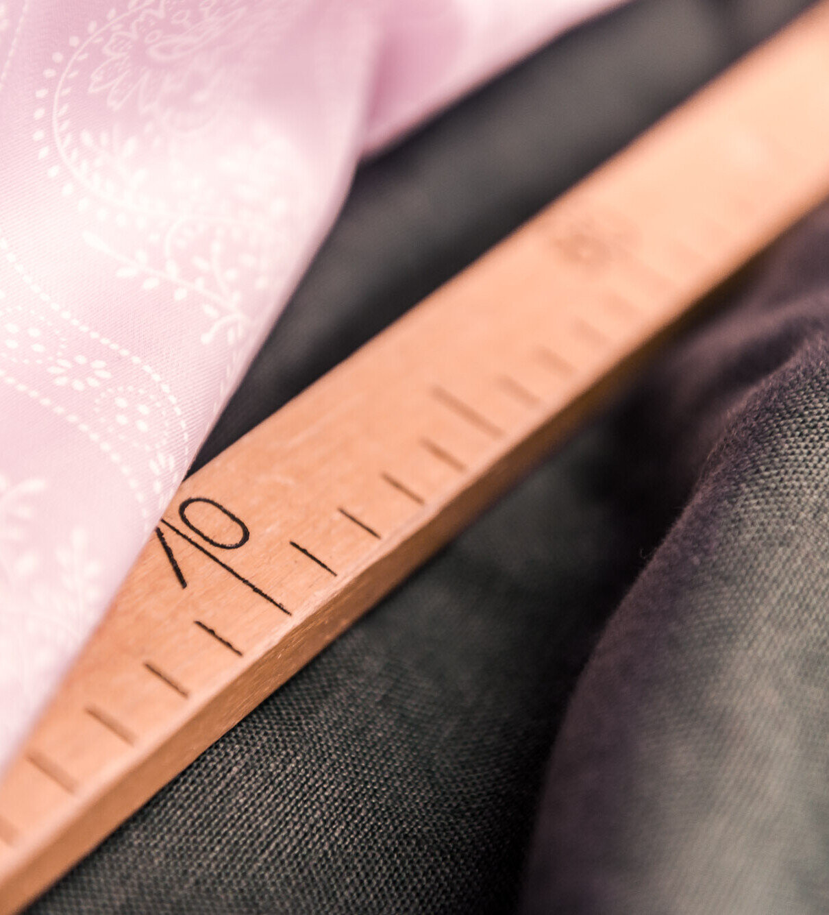 Nahaufnahme eines Holzlineals zwischen rosa gemustertem und dunkelgrauem Stoff – Maßnehmen fürs Nähen.