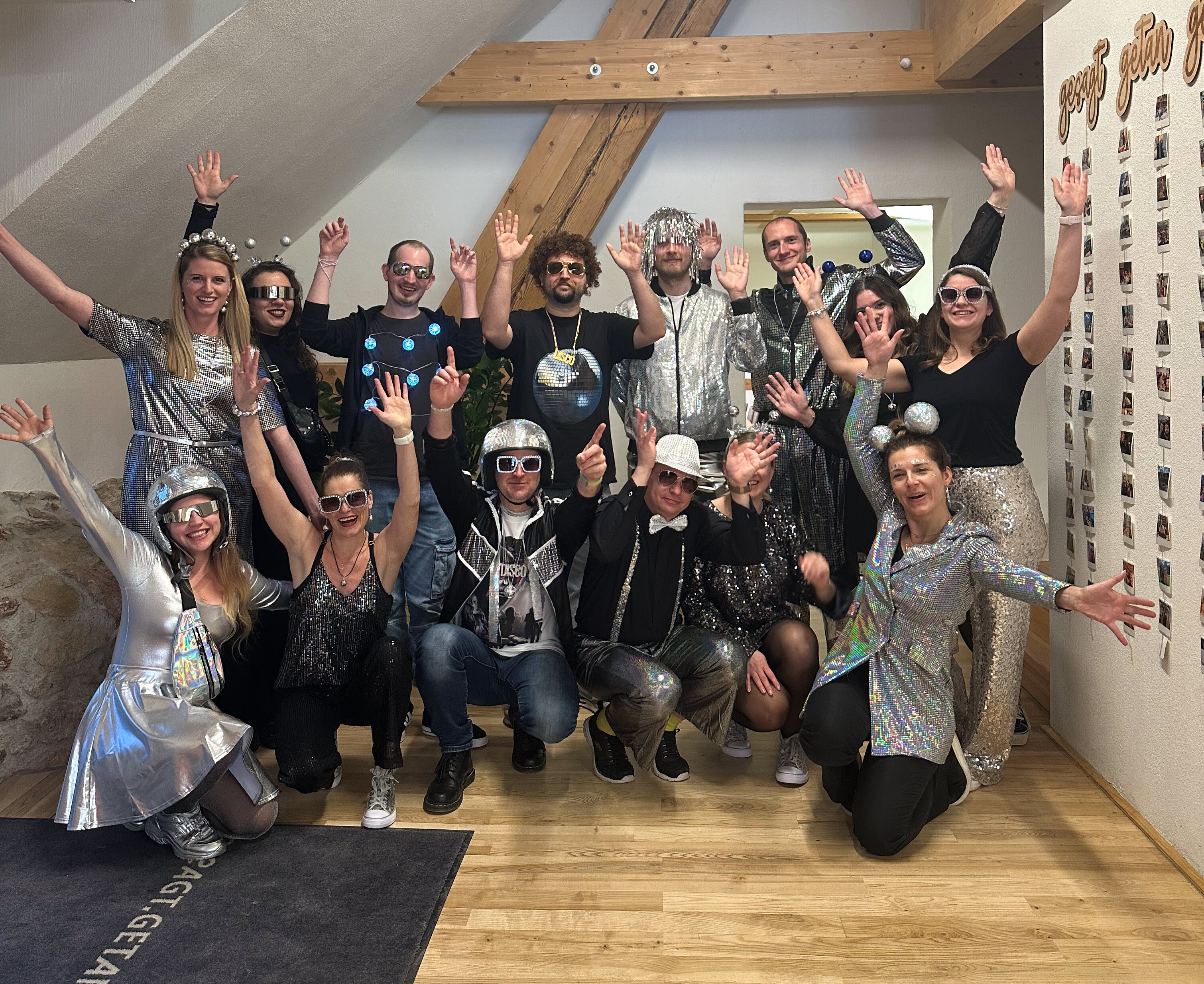 Team im Büro feiert Fasching: Gruppe in silbernen, glitzernden Space- und Disco-Kostümen mit erhobenen Händen.