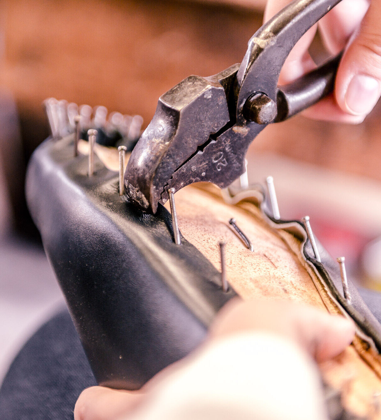 Handwerkliche Schuhreparatur: Mit der Zange werden Nägel aus einer Ledersohle gezogen.